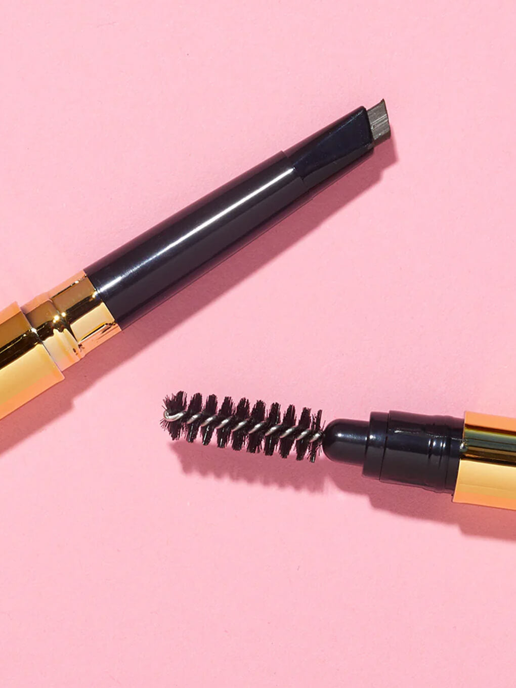 two unibrow universal brow pencils flat lay on pink background